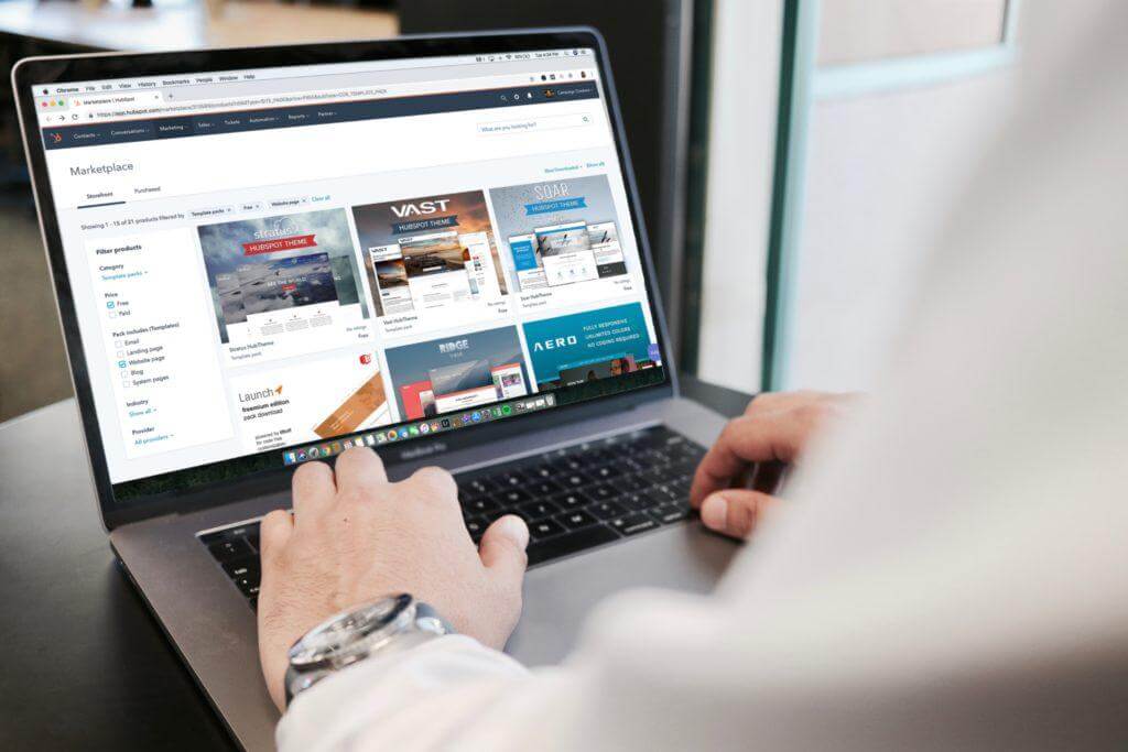 Employee working on laptop with marketing designs loaded on screen.