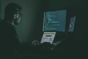 IT employee with headphones on working on laptop and reviewing code.