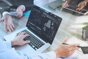 Business investment firm documents on office table with smart phone and laptop and graph financial with social network diagram and three colleagues discussing data in the background.