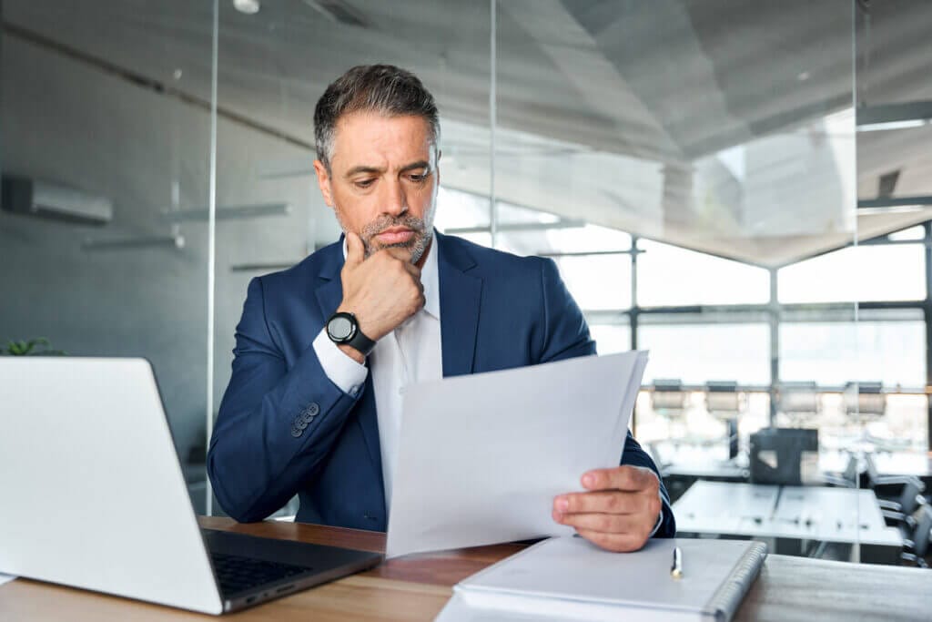 Man in a suit reviewing cybersecurity and IT documentation at his desk.